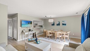A modern living room with a dining area, a TV mounted on the wall, and a view of the outdoors.