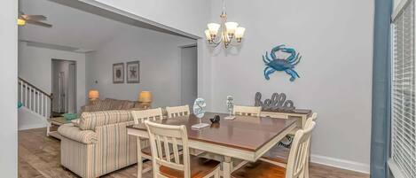 Een eetruimte met een houten tafel en stoelen, een kroonluchter en een blauwe krab decoratie aan de muur.