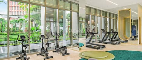 Un gimnasio moderno con máquinas de cardio, un espejo y vistas al exterior con vegetación.