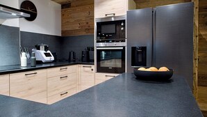 A modern kitchen with wooden cabinets, a black countertop, stainless steel appliances, and a bowl of fruit.