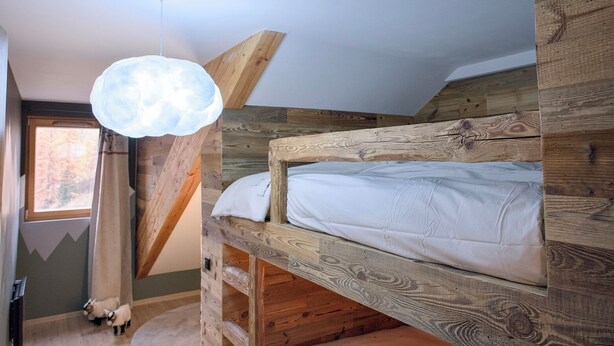A bunk bed with a wooden headboard, a hanging light fixture, and a window with a view of trees.