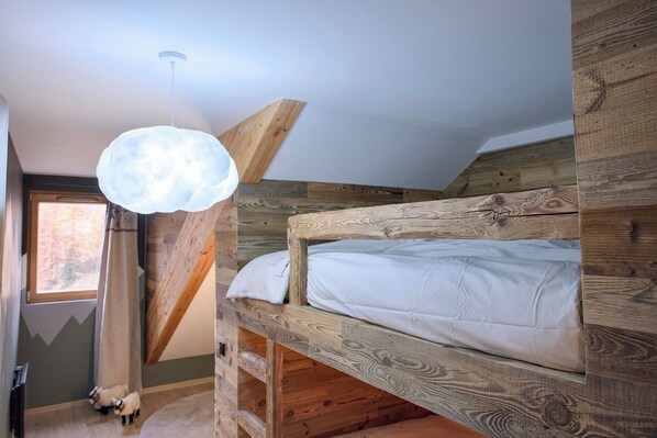 A bunk bed with a wooden headboard, a hanging light fixture, and a window with a view of trees.