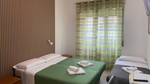 Quarto de hotel com duas camas, parede de painéis de madeira, colcha verde e cortina listrada.