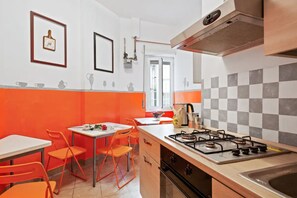 Une cuisine avec un cuisinière à gaz, des chaises orange et un dosseret à carreaux.