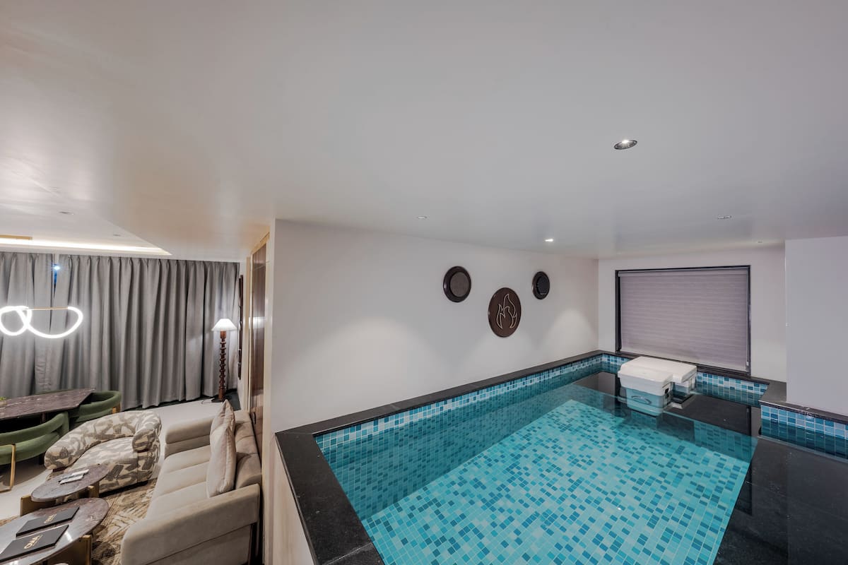 Una piscina interior moderna con suelo de baldosas, un sofá y una mesa con sillas.