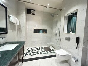 A modern bathroom with a marble floor, a glass-enclosed shower, a sink with a green countertop, and a toilet.