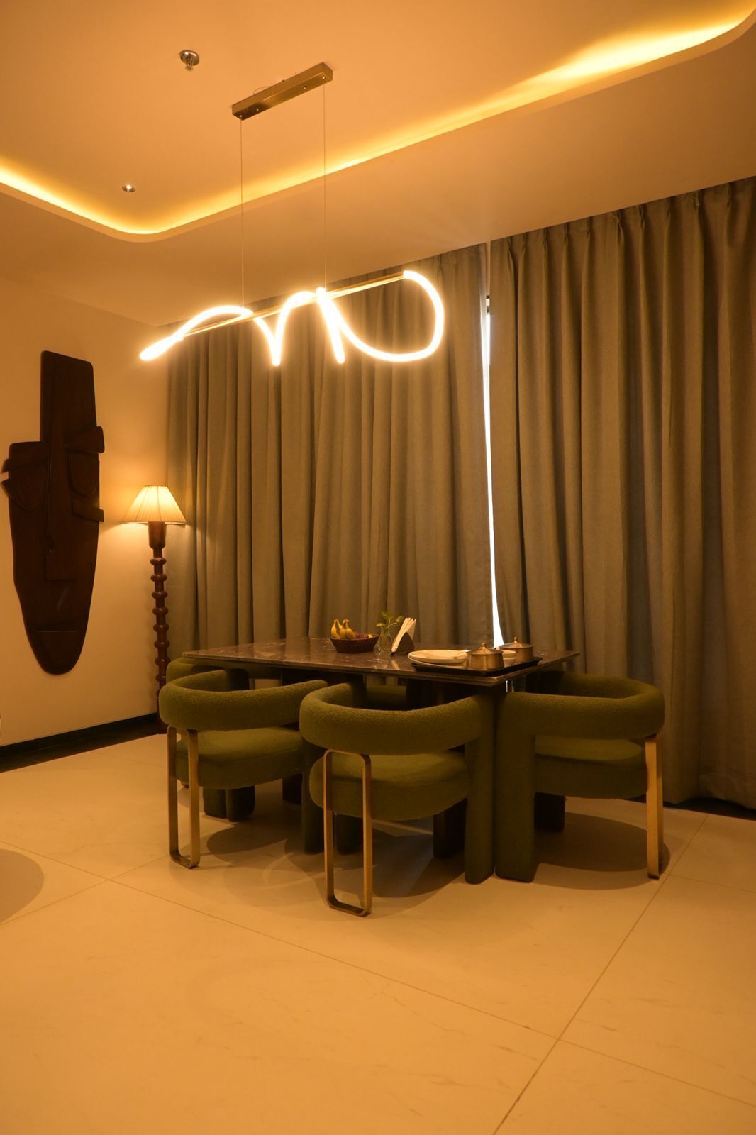 A modern dining area with a round table, green upholstered chairs, and a unique ceiling light design.