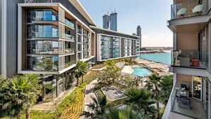 Ein modernes Hotel mit mehreren Balkonen, einem Swimmingpool und Blick auf das Meer sowie nahegelegene Gebäude.