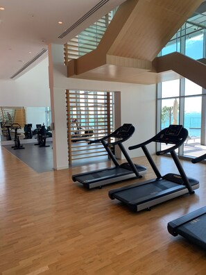 Ein Fitnessraum mit Laufbändern, Ergometer und einer Treppe, die zu einem Balkon mit Aussicht führt.