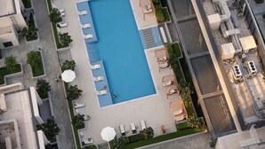 An aerial view of a hotel with a rectangular swimming pool surrounded by lounge chairs and umbrellas. - Astonishing 1 BR Apartment in Creek Harbour (Dubai)