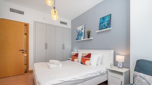A modern bedroom with a large bed, a bedside table with a lamp, a wardrobe, and artwork on the wall. - Spacious 3BR Marina Stay With City Views (Dubai)