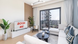 A modern living room with a sofa, coffee table, and a TV displaying "BOOK ME". - Chic 1-bed for 4 in Prime Dubai Hills Location (Dubai)
