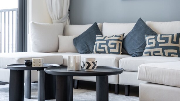 A modern living room with a white sofa, two black round tables, and decorative pillows. - Chic 1-bed for 4 in Prime Dubai Hills Location (Dubai)