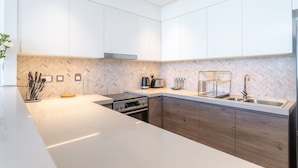 A modern kitchen with white cabinets, a herringbone-patterned backsplash, stainless steel appliances, and a wooden countertop. - Bright Elegant 2BR in Creek Harbour (Dubai)