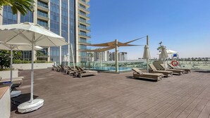 A rooftop pool area with sun loungers, umbrellas, and a view of high-rise buildings. - Bright Elegant 2BR in Creek Harbour (Dubai)