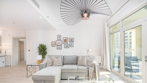 Un salon moderne avec un canapé d’angle, une table basse en verre et une grande fenêtre donnant sur des immeubles.