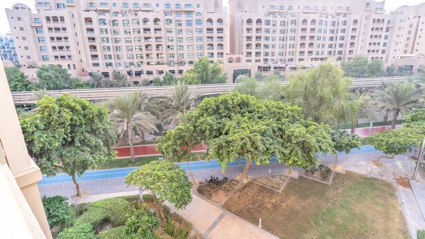 Un hôtel à plusieurs étages doté de balcons, une cour intérieure arborée et un chemin bleu.