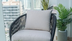 A balcony with a wicker chair and a potted plant. - Glamorous 1BR Apartment - Steps From the Beach (Dubai)