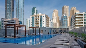 A rooftop pool with lounge chairs and a pergola, surrounded by high-rise buildings. - Glamorous 1BR Apartment - Steps From the Beach (Dubai)