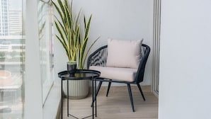 A balcony with a black chair, a round table, and a potted plant. - Glamorous 1BR Apartment - Steps From the Beach (Dubai)