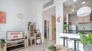 Un salon moderne avec une télévision, une table basse et un canapé. Il y a également un coin cuisine équipé d’un réfrigérateur, d’un évier et de tabourets de bar.