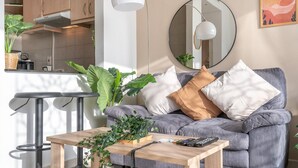 Un salon moderne avec un canapé gris, une table basse en bois et un coin cuisine doté de placards et d’un four à micro-ondes.