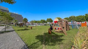 A playground with swings and slides, surrounded by grass and trees, with a building in the background. - Relaxing 3BR in Palm Jumeirah With Beach Views (Dubai)
