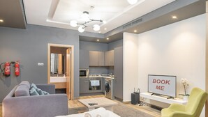 Ein modernes Hotelzimmer mit einem Bett, einem grauen Sofa, einem grünen Sessel, einem Fernseher und einer Küchenzeile.