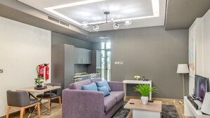 Una sala de estar moderna con un sofá, una mesa de centro y un televisor. Se observa un área de cocina al fondo.
