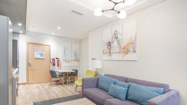 Ein modernes Wohnzimmer mit einer Couch, einem Couchtisch und einem Essbereich mit Stühlen. Eine Tür mit einem Schild, ein Feuerlöscher und Kunstwerke sind an der Wand zu sehen.