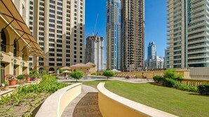 A residential area with high-rise buildings, a well-maintained lawn, and a pathway leading to a building with a yellow facade. - Steps by the Beach - Serene Studio in JBR (Dubai)
