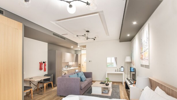 A modern hotel room with a bed, a sofa, a desk, and a kitchenette. - Steps by the Beach - Serene Studio in JBR (Dubai)