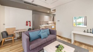 A modern living room with a purple sofa, a coffee table, and a dining area with a table and chairs. A kitchen is visible in the background. - Steps by the Beach - Serene Studio in JBR (Dubai)