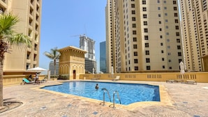 A swimming pool area with tiled flooring, lounge chairs, and a palm tree. - Great 2BR Apartment Near JBR Beach (Dubai)