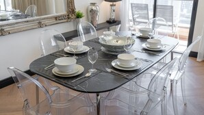 A dining table set with clear chairs, white plates, and a decorative bowl. - Great 2BR Apartment Near JBR Beach (Dubai)
