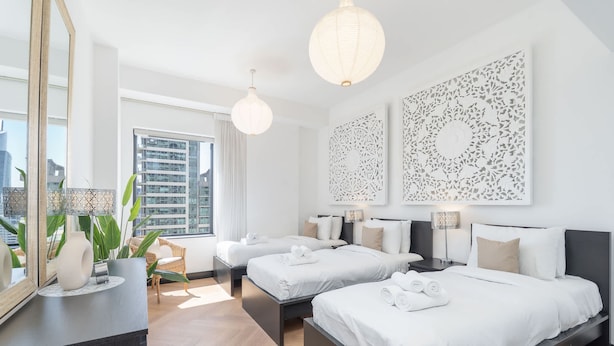A modern hotel room with two beds, a large mirror, and decorative wall art. - Great 2BR Apartment Near JBR Beach (Dubai)