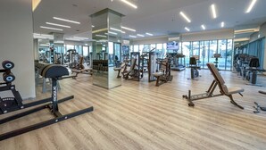 A modern gym with various exercise equipment, large windows, and a wooden floor. - Stylish Cozy 3-bedroom Apartment With Harbour Views in Dubai Creek Harbour (Dubai)