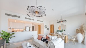 A modern living room with a sofa, a dining table, and a kitchen area in the background. - Stylish Cozy 3-bedroom Apartment With Harbour Views in Dubai Creek Harbour (Dubai)