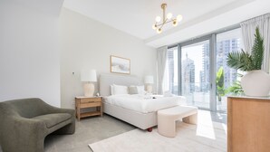 Ein modernes Schlafzimmer mit einem großen Bett, einem grünen Sessel, einem Nachttisch aus Holz und einem großen Fenster mit Blick auf die Stadt.