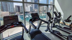 Ein Fitnessstudio mit Laufbändern und Fahrrädern, große Fenster mit Blick auf eine städtische Marina.