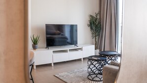 A modern living room with a flat-screen TV on a white entertainment unit, a round black side table, a beige sofa, a patterned rug, and a potted plant. - Chic 1BR Flat Stunning Views in Dubai Hills (Dubai)