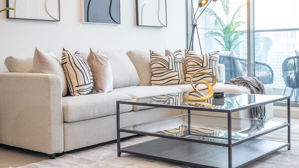 Een moderne woonkamer met een bank, een glazen salontafel en abstracte wandkunst.