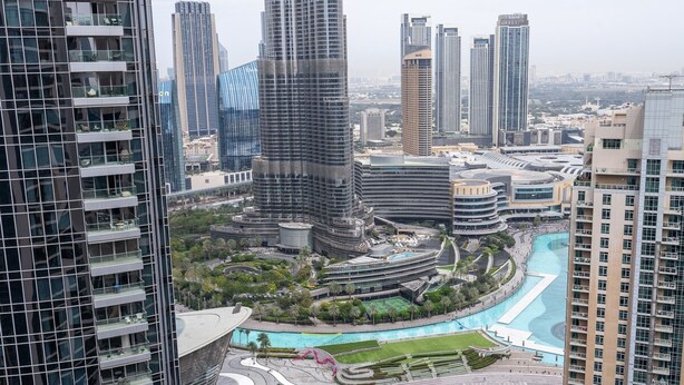 A high-rise building with a curved glass facade, surrounded by other tall buildings and a landscaped area with pathways and greenery. - Luxurious 3-bedroom Apartment in Downtown Near Burj Khalifa in Dubai Mall (Dubai)