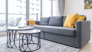 Un salon moderne avec un canapé gris, deux coussins jaunes et une table ronde aux pieds en métal.