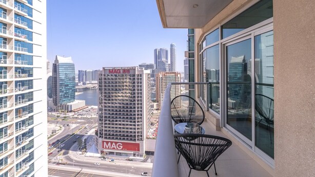 Un balcon offrant une vue sur le paysage urbain, avec notamment un immeuble sur lequel on peut voir une enseigne « MAG ».