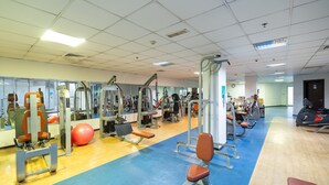 A gym with various exercise equipment, a blue and yellow floor, and a large mirror wall. - Amazing 4-bedroom Apartment Perfect for Families in Dubai Marina (Dubai)