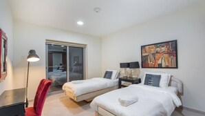 A hotel room with two beds, a desk, a chair, and a painting on the wall. - Scenic 2BR Near Beach in Princess Tower Marina (Dubai)