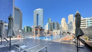 Et tag med swimmingpool, liggestole og parasoller, omgivet af høje bygninger.
