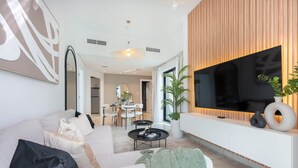 Un salon moderne doté d’un grand téléviseur à écran plat, d’un canapé, d’une table basse et d’un coin repas à l’arrière-plan.