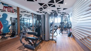 Une salle de sport moderne dotée de divers appareils d’exercice, d’un plancher en bois et d’un plafond au design géométrique.